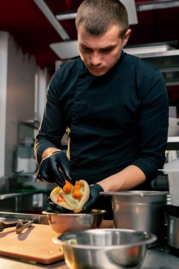 Siyah eldivenli bir şef diğer malzemelerin üstüne ekmekli karides koyar.