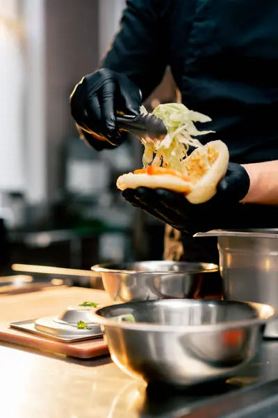 Close Chef Kok Zwarte Handschoenen Zet Verschillende Ingrediënten Een Broodje — Stockfoto