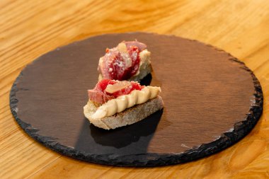 Etli, tuzlu ve peynirli sandviçin siyah bir taş tahtaya güzelce yayılmış halinin yakın çekimi.