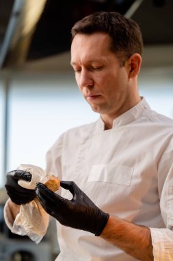 Bir şefin elleri siyah eldivenlerle bir torbadan bir parça ekmeğe sos dökerken yakın plan fotoğrafı.