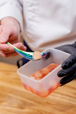 Yuvarlak elma turşusunu krom kaşıkla çıkarmaya yakın plan.