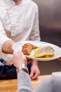 Şefin elleri beyaz tabakta bitmiş balık tabağını garsona uzatıyor.