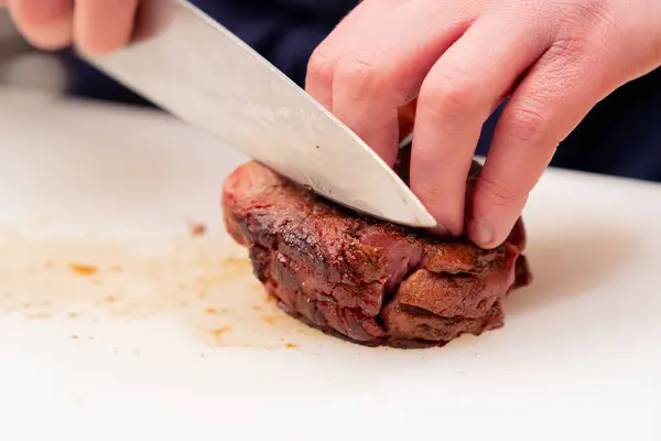 close-up of professional cutting seared beef steak with knife on white board