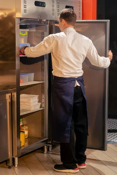 プロのキッチンシェフが冷蔵庫を調べて食材を選ぶ — ストック写真