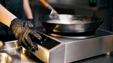 Profesyonel bir mutfağa yakın plan siyah üniformalı bir şef fırını tavayla yakar.