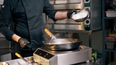 Profesyonel bir aşçı sobanın yanında durur ve sıcak bir kızartmaya yemek atar.