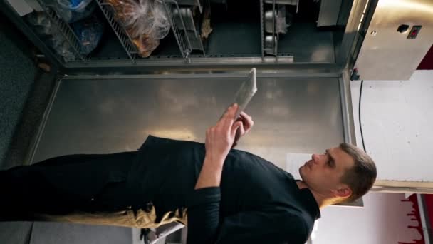 垂直录像一个穿着黑色制服的厨师在一个专业厨房里 查看冰箱里的菜单上的内容 — 图库视频影像