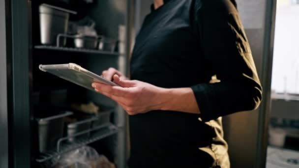 把厨师关在一间穿着黑色制服的专业厨房里 查看冰箱里的食物清单 — 图库视频影像