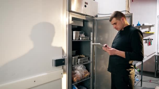 Kuchař Stojí Profesionální Kuchyni Černé Uniformě Dívá Seznamu Ledničce — Stock video