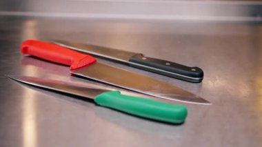 Profesyonel bir mutfakta metal bir masanın üzerinde duran büyük bıçakların yakın plan çekimi.