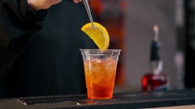 Bar tezgahında genç bir kızın cımbızla bir kokteyle portakal dilimleri eklerken yakın plan fotoğrafı.