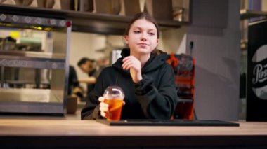 Dirsekleriyle barın arkasında dikilen üzgün kokteyl içip etrafa bakınan bir kızın yakın çekimi.