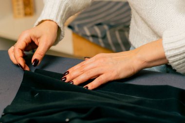 Bir dikiş atölyesine yakın plan. Bir terzi, kıvrım için siyah kumaş iğnelemiş.