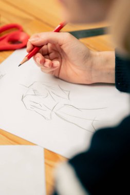 Bir dikiş atölyesine yakın plan bir kadın eli gelecekteki kıyafetlerin bir taslağını çizer.