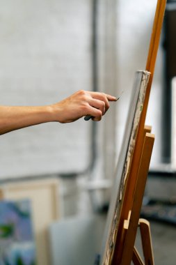 Bir sanat atölyesinde mavi tişörtlü bir sanatçı palet bıçağıyla geniş bir vuruş yapar.