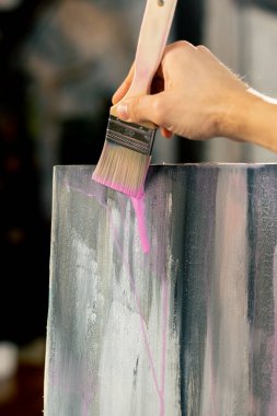 Aşağıdaki bir sanat atölyesinde sanatçı tuvalde pembe çizgiler çiziyor.