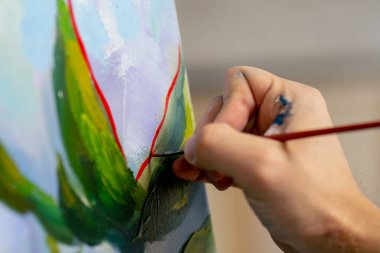 Bir sanat stüdyosunda çiçeklerle resim yapan sanatçı, resmin detaylarını kırmızı boyayla çiziyor.