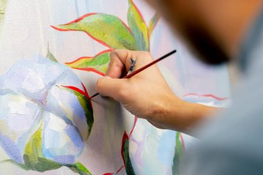 Bir sanat stüdyosunda çiçeklerle resim yapan sanatçı, resmin detaylarını kırmızı boyayla çiziyor.