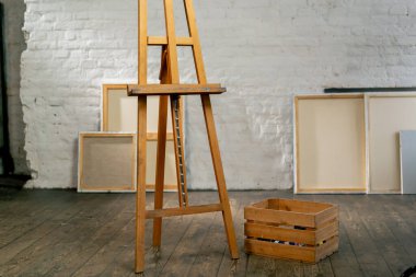 Bir sanat stüdyosunda, bir kutunun yanında tuvallerin arka planına karşı bir tripod vardır.