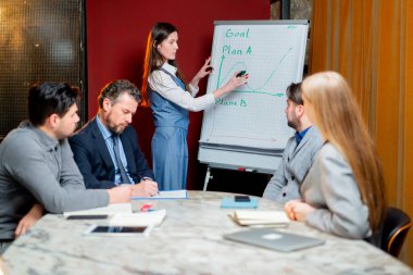 Ofis çalışanları kırmızı duvarlı bir konferans odasında müdürün başkanlığında aktif olarak programı tartışıyorlar.
