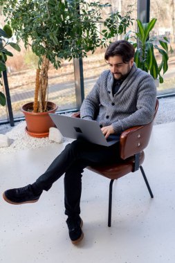 Bilgisayarda çalışan genç bir ofis çalışanının arka planda oturan bir sandalyenin üzerinde oturması.