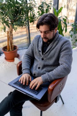 Bilgisayarda çalışan genç bir ofis çalışanının arka planda oturan bir sandalyenin üzerinde oturması.