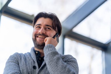 Bir ofis çalışanı pencerenin yanında durmuş gülümseyen bir iş konuşması yapıyor.