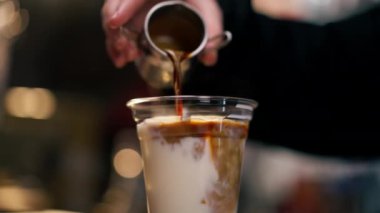 Bar tezgahına yakın plan bir kız kapuçino makinesinden kahveyi sütlü plastik bardağa dolduruyor.