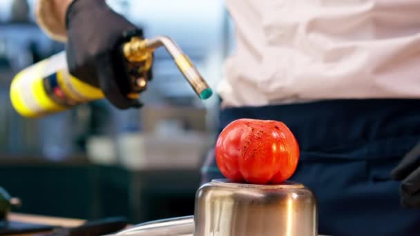 厨师戴着黑色手套站在厨房里 手里拿着一个燃烧器 把西红柿烧着 — 图库视频影像