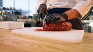 Siyah eldivenli bir şefin eli, tahtada bir parça çiğ et keserken yakın plan fotoğrafı.