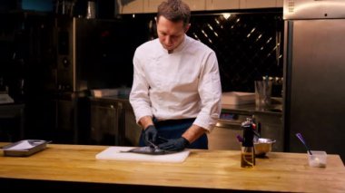 Profesyonel bir mutfakta beyaz ceketli bir şef pişirmeden önce balığı bıçakla keser.