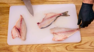 Profesyonel bir mutfakta beyaz ceketli bir şef pişirmeden önce bıçakla balık keser.