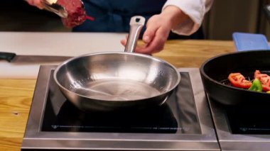 Şefin elinin yakın plan fotoğrafı. Bifteği kızartma tavasına maşayla koyuyor.