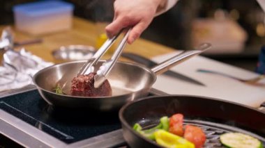 Şefin elinin yakın plan fotoğrafı. Bifteği kızartma tavasına maşayla koyuyor.