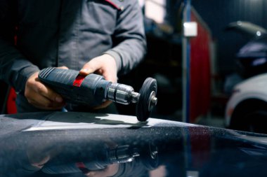 Benzin istasyonunda bir araba tamircisi arabanın bir parçasını zımparalamaya çalışıyor.