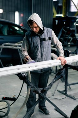 Benzin istasyonundaki oto tamircisi beyaz bir arabanın ön tarafını cilalıyor.