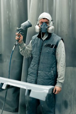 Bir benzin istasyonunda araba parçaları boyama ustası elinde sprey silahla kameraya bakıyor.