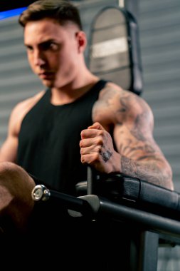 Spor salonunda genç ve yakışıklı bir adam dövmeleri ile karın kaslarını yatay çizgiye pompalıyor.