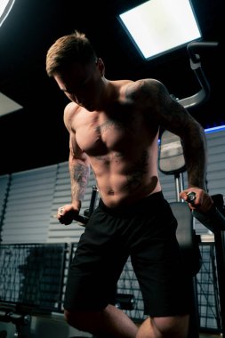 Spor salonunda dövmeli genç yakışıklı adam kendini yukarı çekti ve kollarını yatay çubuğa koydu.