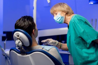 Dişçi kliniğinde genç bir adam yeşil üniformalı bir dişçiye danışmanlık yapıyor.