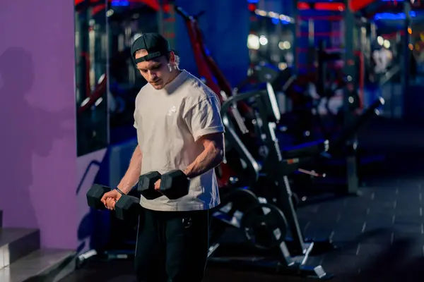 Spor Salonunda Tişörtlü Şapkalı Genç Yakışıklı Bir Adam Dambıllarla Egzersiz — Stok fotoğraf