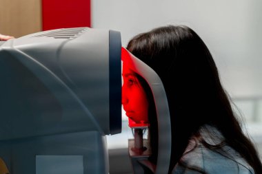 Bir göz doktoru kliniğinde küçük bir kız kırmızı ışık makinesiyle görme yeteneğini teşhis ediyor.