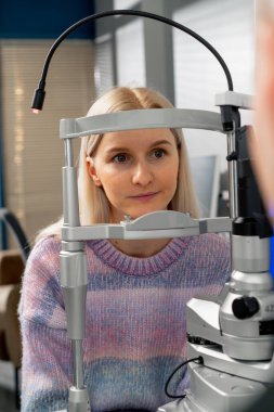 Bir oftalmoloji kliniğinde genç bir kız teşhis cihazı aracılığıyla doktorla iletişim kurar.