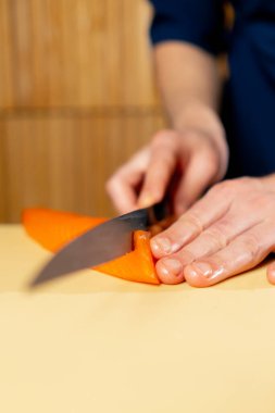 Japon restoranına yakın mavi üniformalı bir şef sarı tahtada suşi için balık keser.