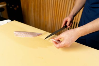 Japon restoranına yakın mavi üniformalı bir şef sarı tahtada suşi için balık keser.