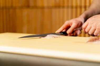 Japon restoranına yakın mavi üniformalı bir şef sarı tahtada suşi için balık keser.