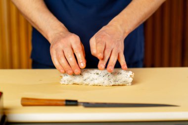 Japon lokantasında mavi üniformalı bir şef sarı bir tahtanın üzerinde balık sarması çeviriyor.