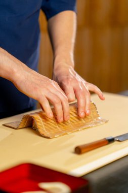 Japon lokantasında mavi üniformalı bir şef sarı bir tahtanın üzerinde balık sarması çeviriyor.