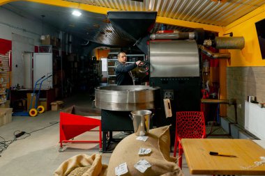 Küçük bir kızartma fabrikasında bir işçi kızartma makinesinin yanında duruyor ve kızarma derecesini izliyor.