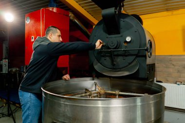 Küçük bir kızartma fabrikasında bir işçi kızartma makinesinin yanında duruyor ve kızarma derecesini izliyor.